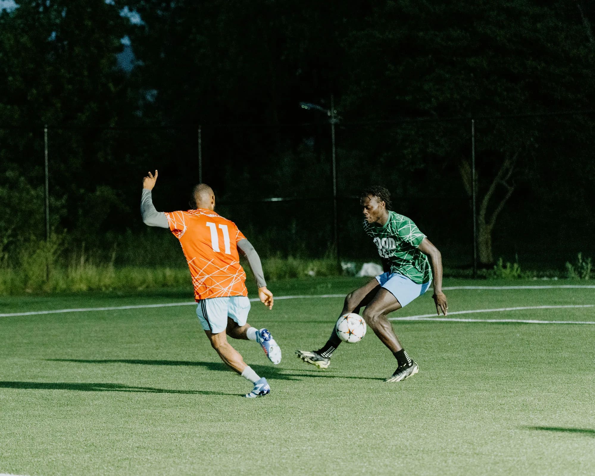 Two players competing for the ball in a GoodRec pickup soccer game at dusk